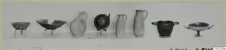 Eight vessels from Tomb 49 at Marion lined up in a row against a plain background, bowls, jugs and cups.