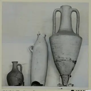 Three pottery vessels on a shelf: a small one-handled jug, a tall narrow vessel with a broken base, and a large two-handled amphora.