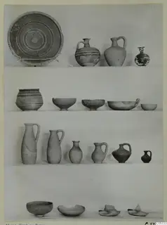 Pottery from Marion, Tomb 23: plates, jugs, jars and bowls arranged in four rows against a plain backdrop.