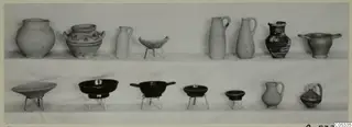 Two rows of pottery jugs and bowls from Marion Tomb 57, set out on a pale surface.