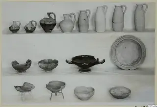 Pottery from Marion, Tomb 61: rows of jugs, bowls and a plate, with two bowls set on wire stands.