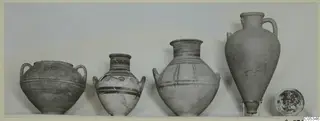 Four pottery vessels and a small dish from Tomb 94 at Marion, standing in a row on a pale surface