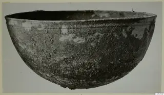 Corroded metal bowl from Marion, Tomb 22, seen from the side against a pale background.