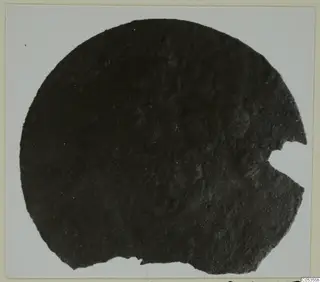 Corroded metal disc with a broken edge on the right and bottom, photographed on a light card mount, from Marion Tomb 72.