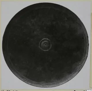 Bronze mirror with a raised central boss and concentric rings near the rim, seen face-on on a pale ground