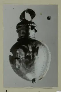 Small metal object with a loop at the top and a ribbed collar, photographed on a card mount.