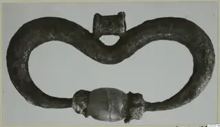 Dark metal loop with a barrel-shaped bead at its lower centre, from Marion
