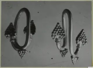 Two gold loop-shaped objects with triangular granulated terminals, photographed on a grey background.