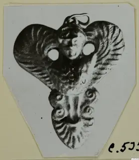 Metal pendant with a small face in relief, two round holes and a loop at the top, from Marion