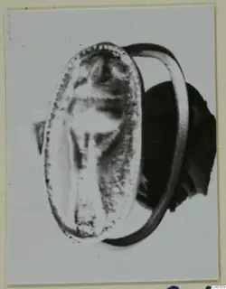 Ring with an oval bezel and a central engraved design, shown large on a card mount.