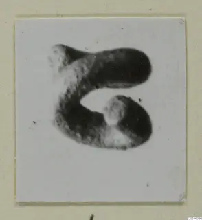 Blurred photograph of a single curved object, a piece of jewellery from Amathus, on a white card mount.
