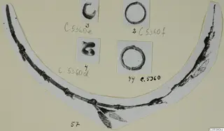 Corroded metal objects on a card: two small rings, two curled pieces, and a long curved fragment on a paper strip.