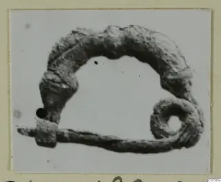 Bronze bow-shaped object with a coiled end and a straight pin, from Amathus, shown on a card mount.