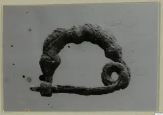 Bronze fibula from Amathus with a coiled spring and long pin, photographed against a plain grey background.