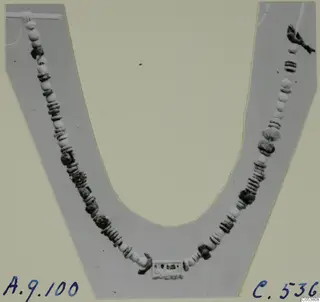 Necklace of pale and dark beads laid in a curve on a grey U-shaped card
