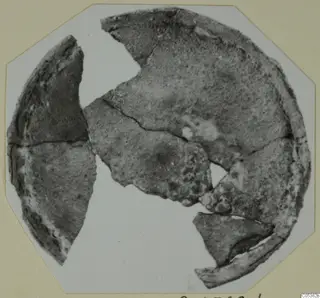 Broken pieces of a round, dark, corroded object from Amathus, shown on a card mount