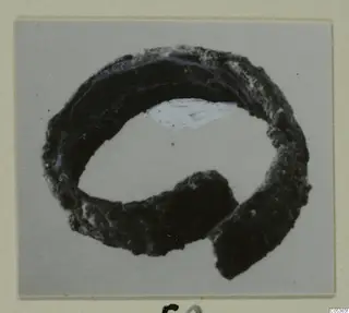 Corroded bronze ring-shaped adornment from Amathus, shown on a grey background with a cream mount.