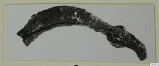 Curved, corroded bronze object from Amathus, shown against a pale ground