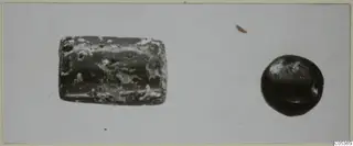 Two stone objects on a pale background: a greenish, mottled cylinder-like object and a smaller dark rounded object