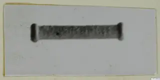 Silver artefact: a blurred dark grey cylinder with rounded ends, shown against a pale plain background