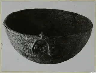 Dark, rounded bowl with a ring handle on its side, photographed on a pale background