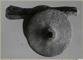 Stone object from Amathus: a round flat disc with a central boss and hole, with an elongated stone piece behind it