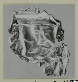 Crumpled fragment of thin sheet with a faint impressed pattern, from Amathus, shown on a grey backing.