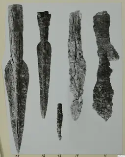 Five corroded iron objects with long tapering blades, laid out in a row on a mounted photograph, from Amathus.
