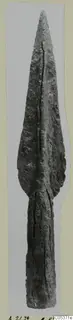 Bronze spearhead with a long leaf-shaped blade and a central rib, photographed upright against a grey backdrop.