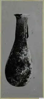Blown glass bottle from Amathus with a long neck, flared rim and teardrop body, its surface dark and weathered.