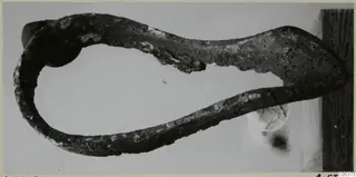 Corroded metal object curved into an open loop with a flattened end, from Amathus, photographed on a plain background.