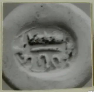 Blurred close-up of an engraved seal or gem face with a horizontal band and looped motifs