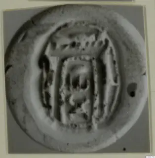 Round seal or impression with a raised rim and a rectangular design in the centre, photographed close up.