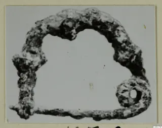 Corroded bronze loop from Amathus: a curved arch-shaped piece with a ring at one end.