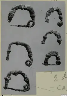 Six corroded bronze arched fibulae with ring ends, from Amathus, shown on a grey background