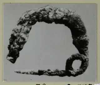 Corroded bronze arched object with a small ring at one end, photographed alone, from Amathus