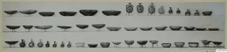 Three rows of pottery bowls, dishes and small jugs set out on shelves against a pale background.