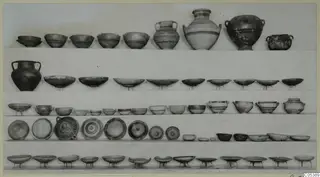 Rows of pottery bowls, handled jars and dishes set out on shelves, Amathus Tomb 16.