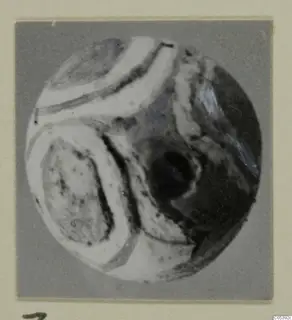 Round object with curving white bands and dark patches, photographed on a grey mount, from Amathus tombs 2-26