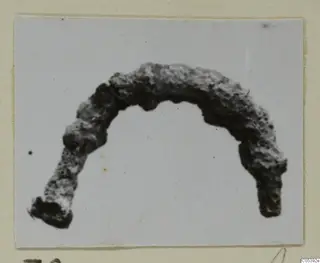 Corroded, arc-shaped metal find from Amathus, photographed on a card mount