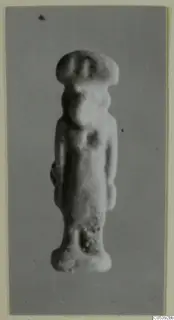 Small standing figurine with a wide flat-topped headdress, photographed against a grey backdrop, from Amathus