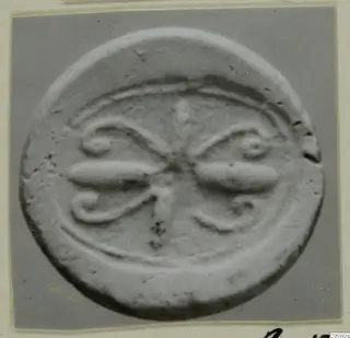 Round seal or impression from Amathus with raised scroll and leaf design, photographed close up.