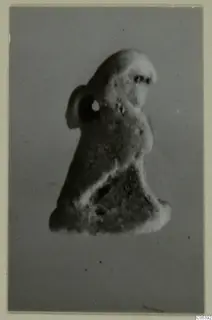 Small figure with a suspension hole through a lug at its side, shown against a grey backdrop