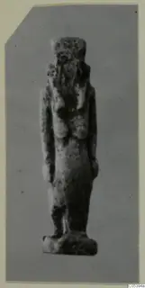 Small standing figure amulet of faience from Marion Tomb 50, shown against a grey backdrop