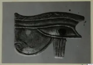 Eye-shaped jewellery piece with a spiral curl and a fluted tab below, photographed against a grey background.