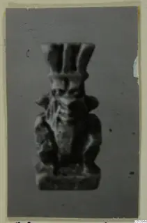 Blurred photograph of a small figurine with a tall headdress, mounted on a grey card