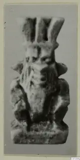Small figure amulet from Marion, Tomb 50, photographed against a grey backdrop