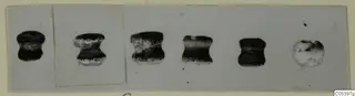 Six small bead-like objects from Tomb 9 at Marion, shown in a row on a pale card mount.