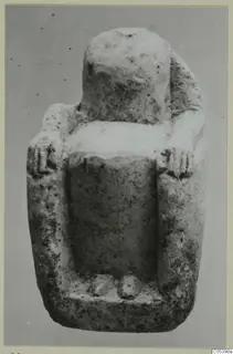 Limestone figurine of a seated figure with a blocky head and short arms, against a plain grey background.