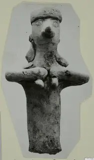 Terracotta figurine with a cylindrical body, arms stretched out to the sides and a flat-topped head with a large nose.